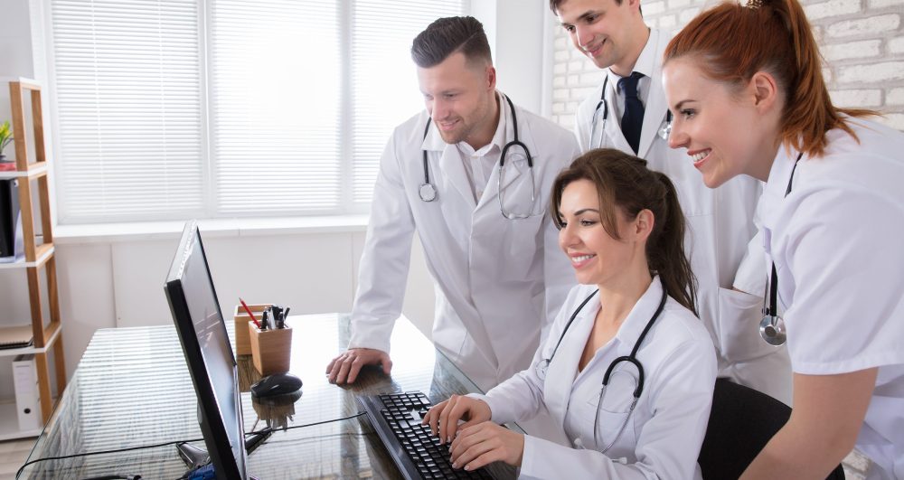 Group Of Smiling Doctors Looking At Computer In Clinic