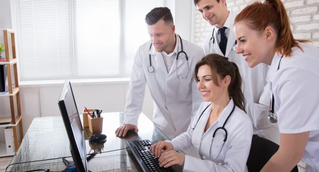 Group Of Smiling Doctors Looking At Computer In Clinic