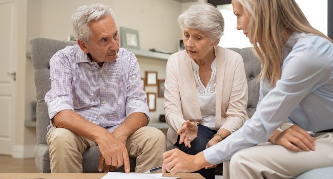 Business agent planning with a retired couple their future investment opportunities. Financial advisor talking to elderly man and woman and pointing the terms of contract on document. Retirement plans